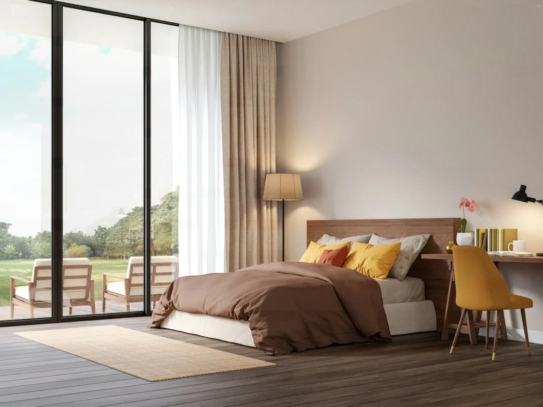 Bedroom with a timber headboard, brown bedding, yellow cushions and desk chair, layered curtains and garden-facing glazing