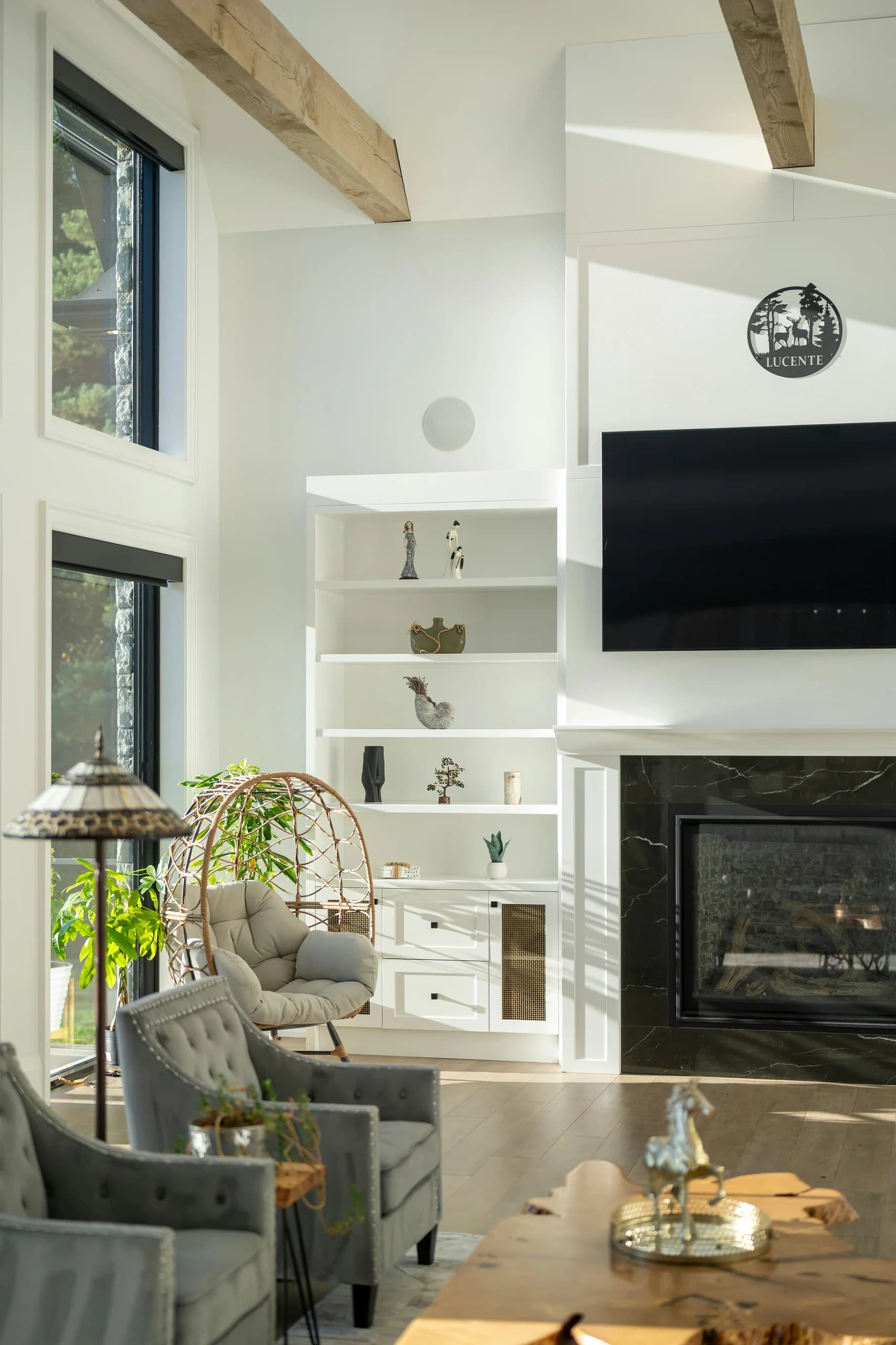 Double-height living-room corner with tall windows, white display shelves, armchairs and a dark fireplace surround