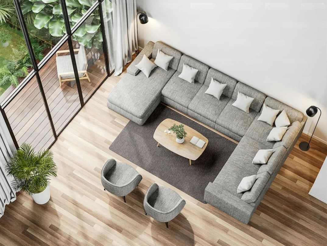 Overhead view of a grey sectional, two occasional chairs and a timber coffee table beside garden-facing glass doors