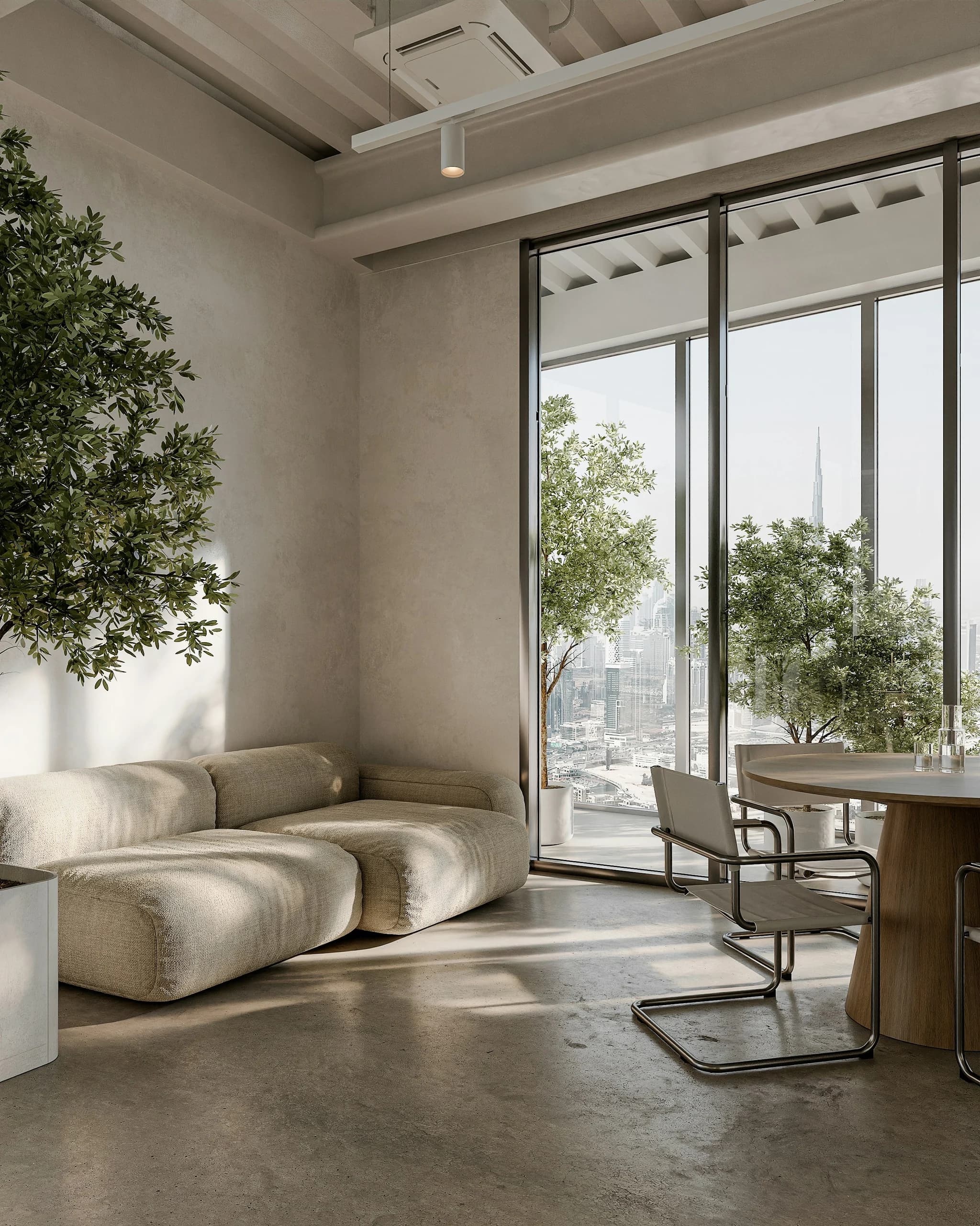 Office lounge with a curved neutral sofa, a round table and chairs, potted trees and full-height city-facing glazing