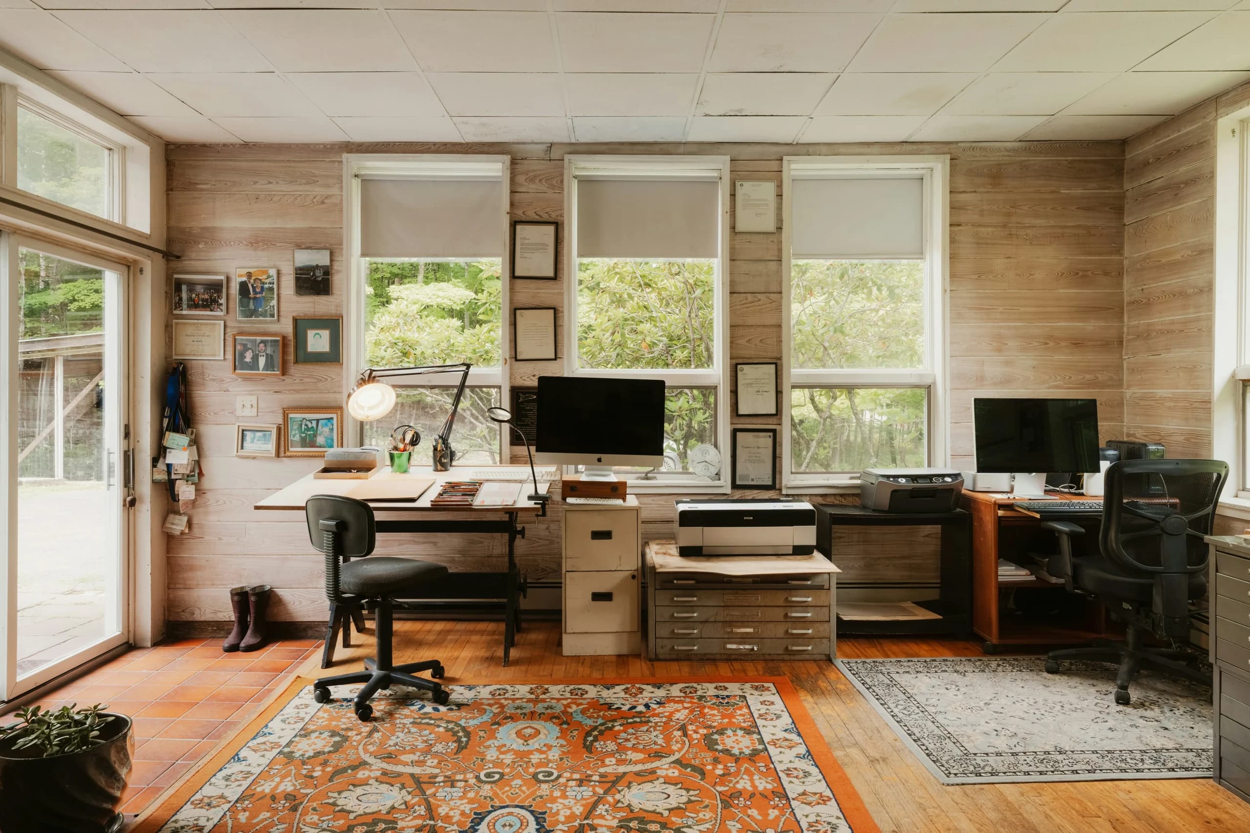 Personal study with two desks and computer screens, timber-clad walls, roller blinds, task lamps and patterned rugs