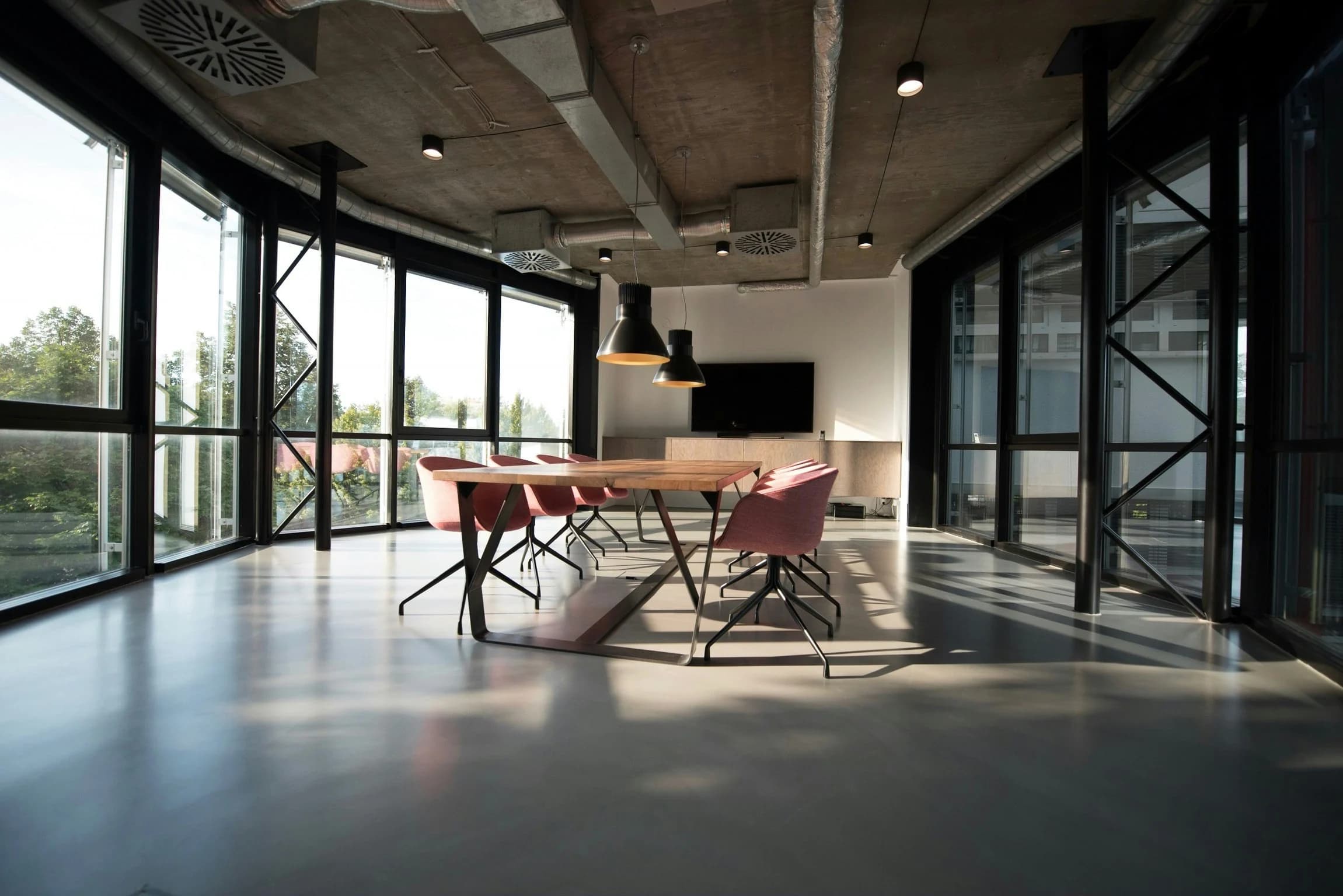 Meeting room with a long timber table, pink upholstered chairs, black-framed glass walls and suspended black lights